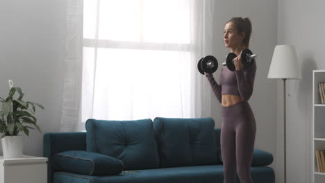 pretty-sportswoman-is-training-with-dumbbells-in-apartment-at-daytime-full-length-portrait-of-athletic-lady-in-apartment-with-modern-interior-healthy-lifestyle-and-fitness
